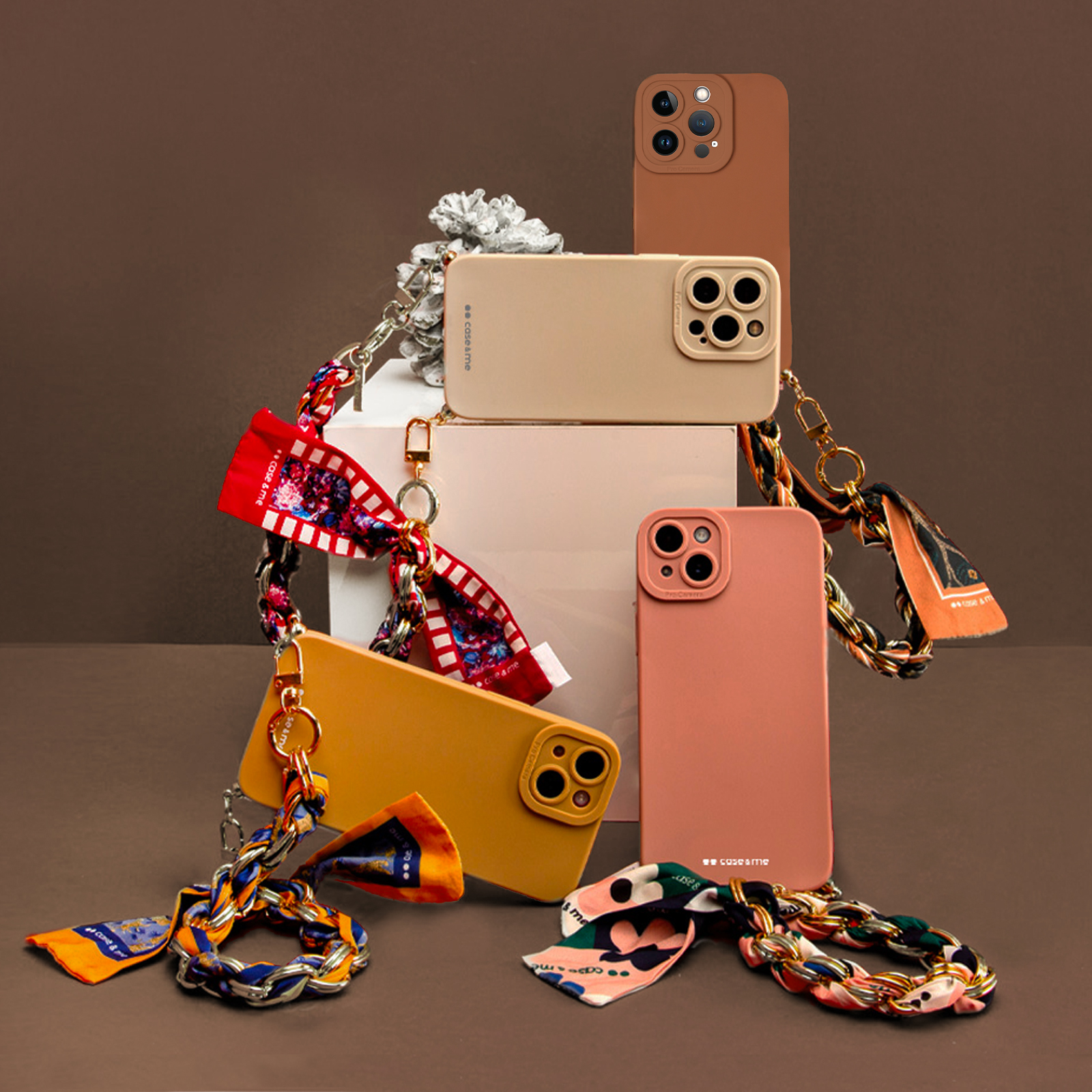 Cuatro fundas de teléfono en tonos marrón, beige, rosa y amarillo con cadenas y pañuelos.