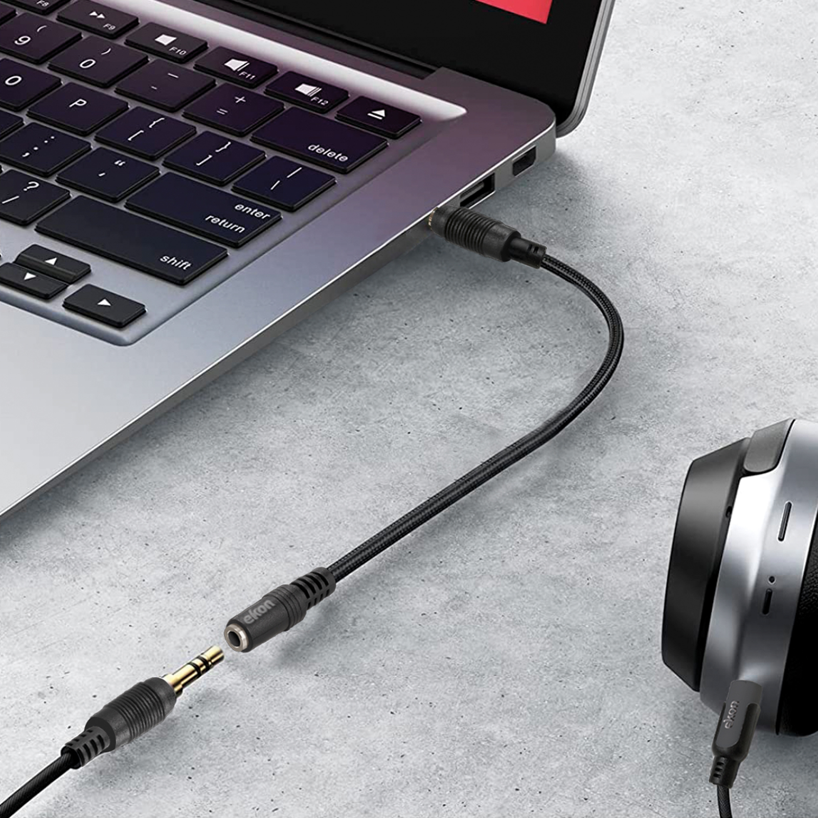 Un cable de audio negro conecta una computadora portátil a auriculares sobre una superficie gris.