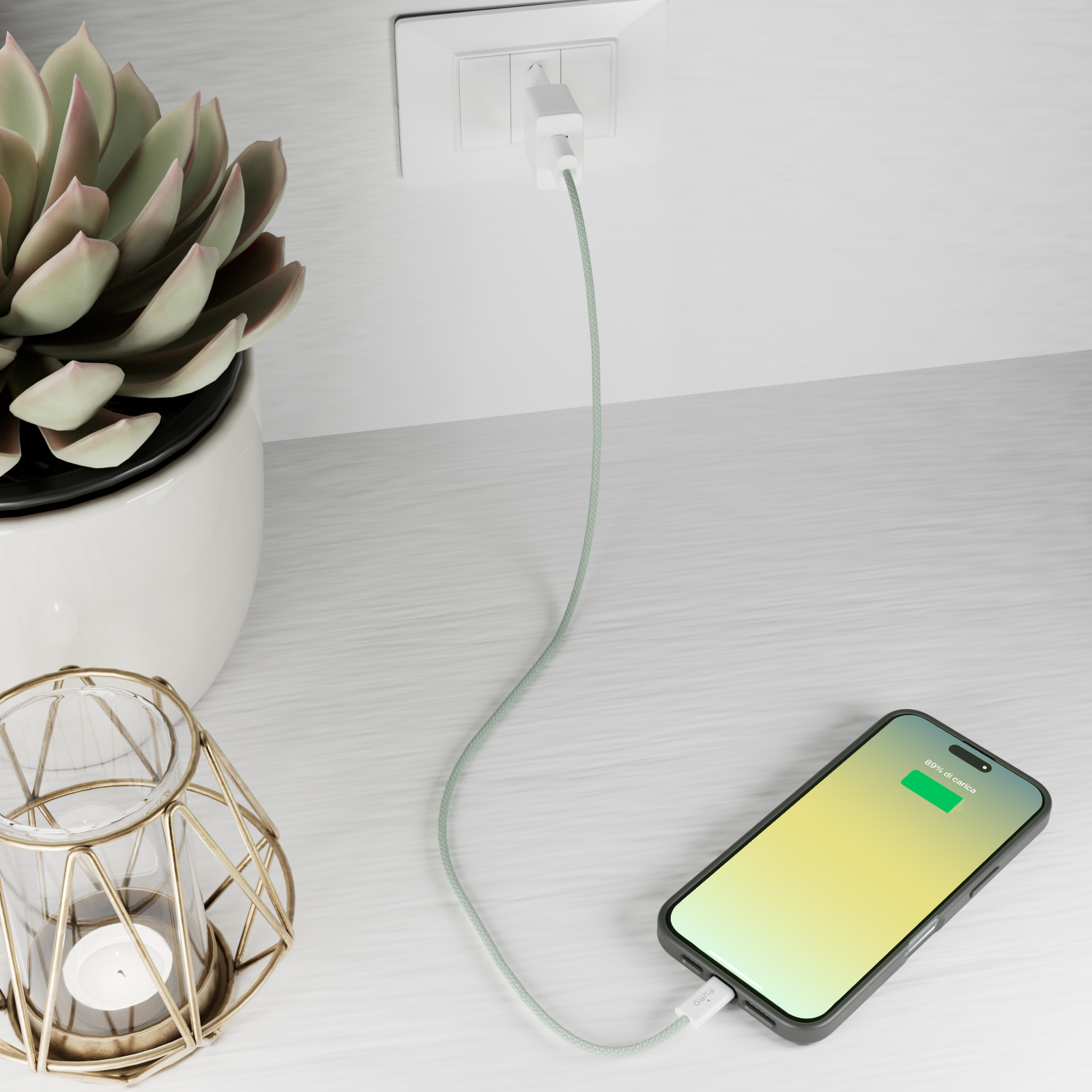 Un telefono si carica a una presa, con una pianta e un portacandele vicini.