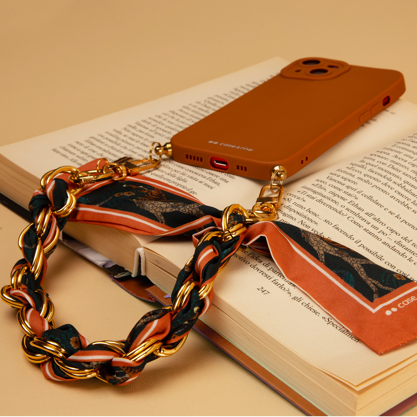 Una funda de teléfono marrón con correa de cadena dorada sobre un libro.