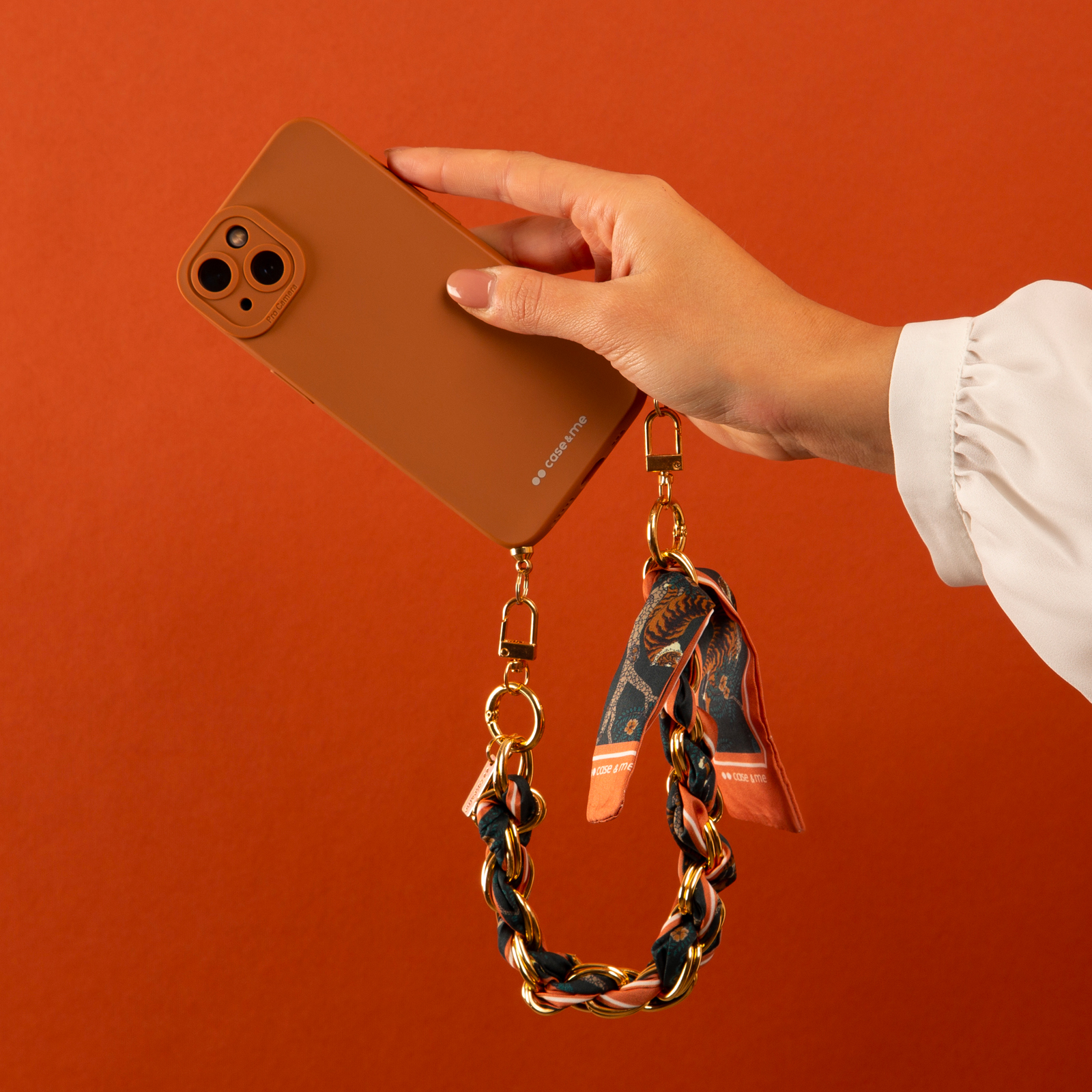 Una mano sujeta un teléfono marrón con una correa de cadena dorada con estampado de tigre.