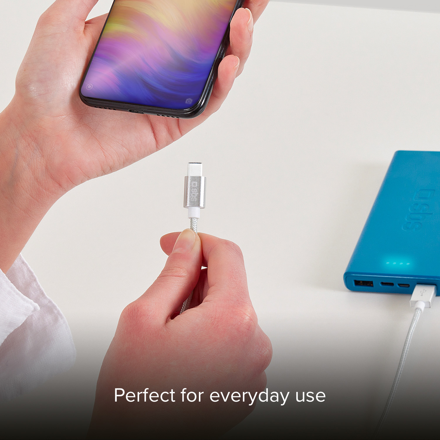 Una mano sostiene un teléfono inteligente mientras otra sostiene un adaptador de carga plateado.