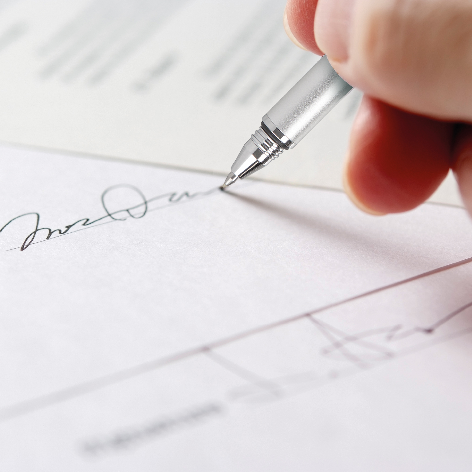 Primer plano de una mano sujetando un bolígrafo plateado, firmando un documento.