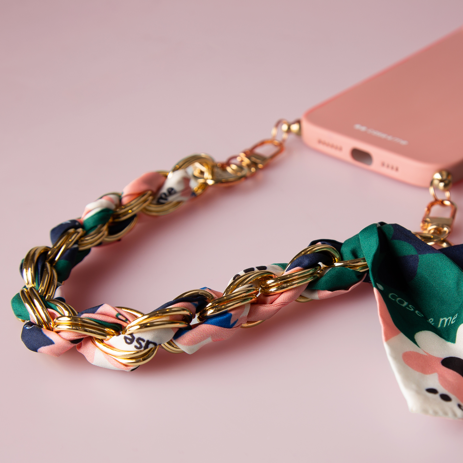Una funda de teléfono rosa con una cadena dorada entrelazada con un pañuelo colorido.