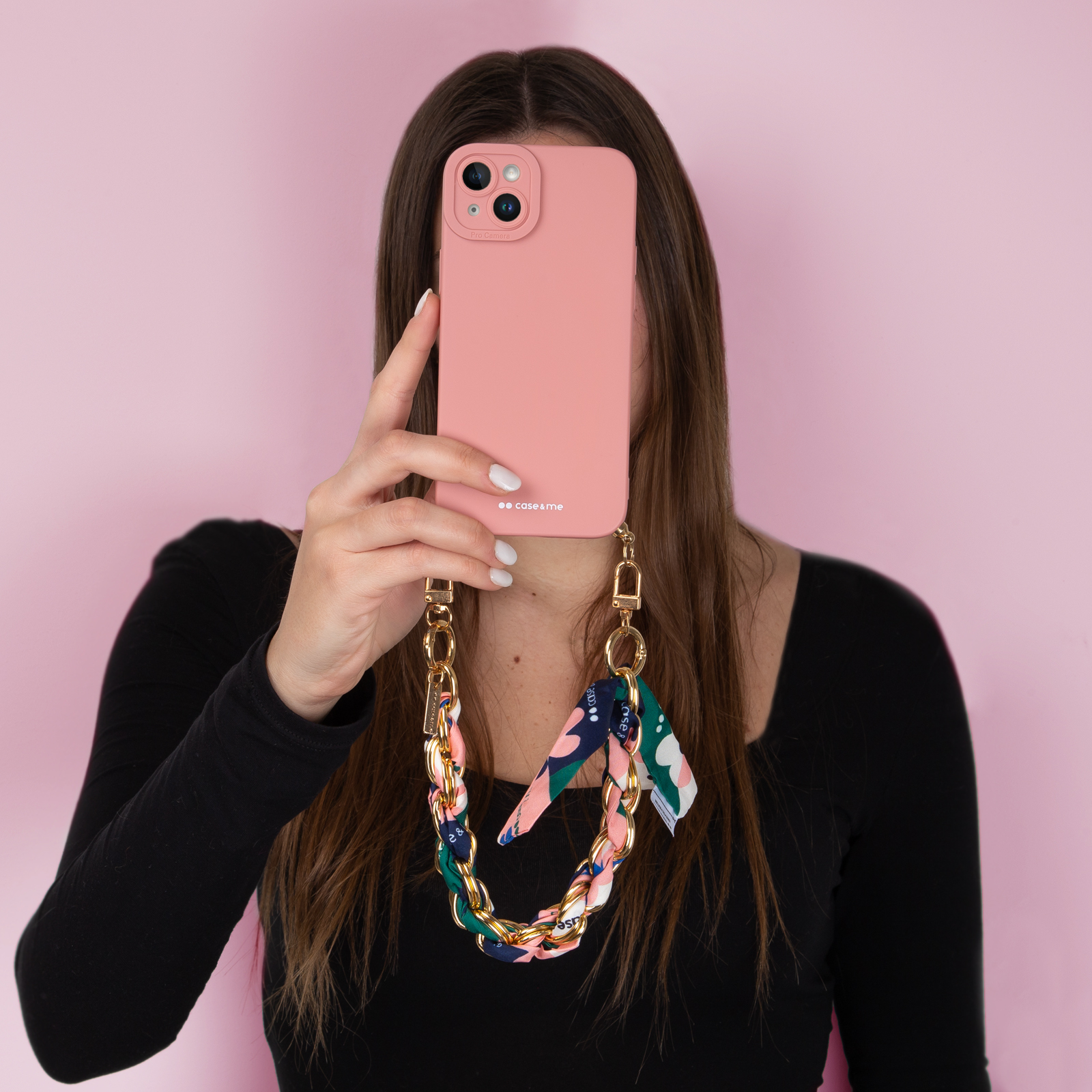 Una mujer sostiene un iPhone rosa con un collar de cadena dorada frente a su cara.