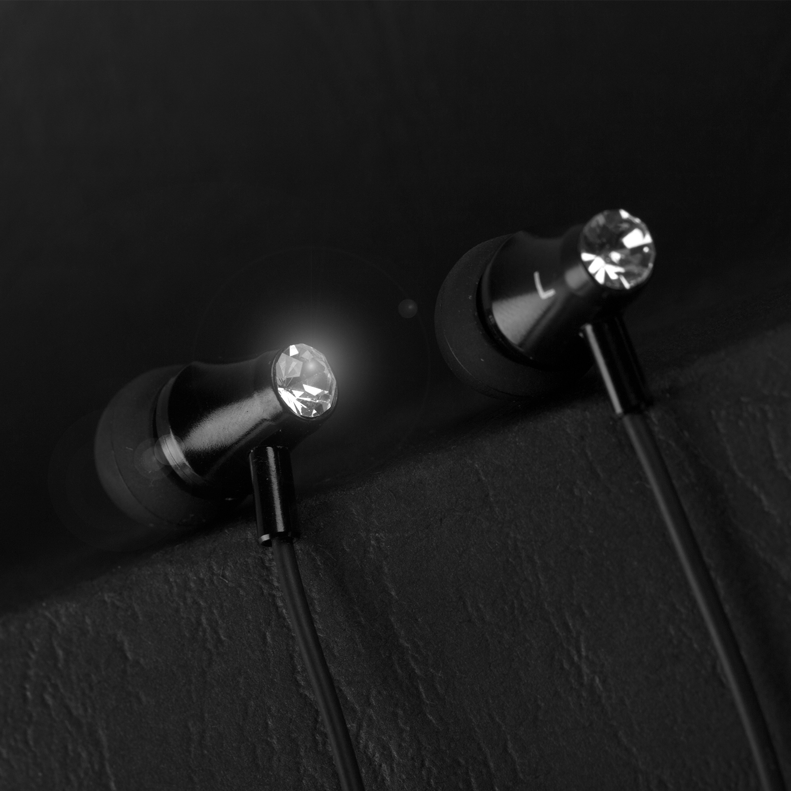 Dos auriculares intrauditivos brillantes con cable negro sobre fondo oscuro.