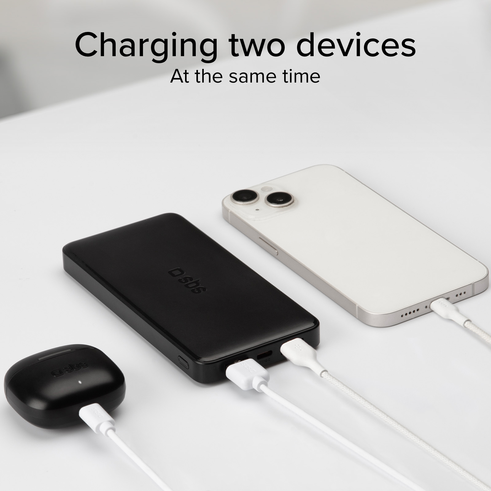 Un power bank nero, una custodia di ricarica bianca e uno smartphone bianco in carica.