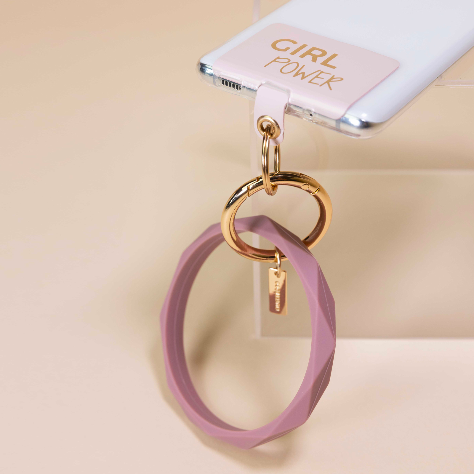 Un llavero de pulsera morada cuelga de un anillo dorado sujeto a un móvil.