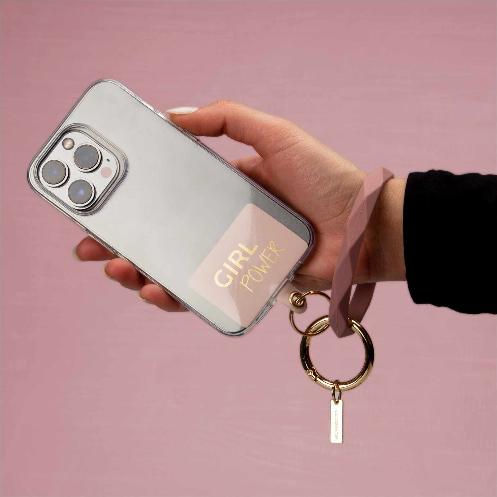 Una mano sostiene un smartphone con una funda transparente y una pegatina de 'GIRL POWER', unido a un llavero de pulsera rosa.