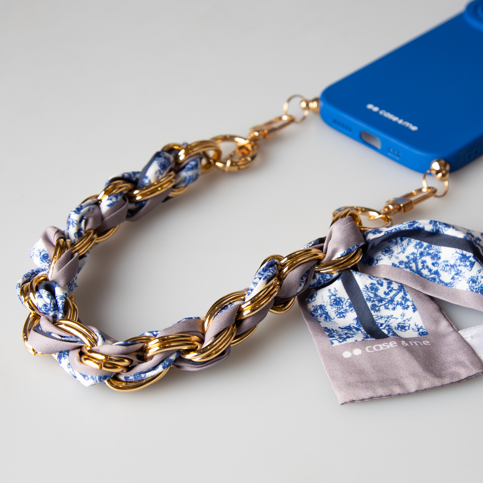 Una custodia blu per telefono con una catena dorata intrecciata con tessuto fantasia blu e bianco.