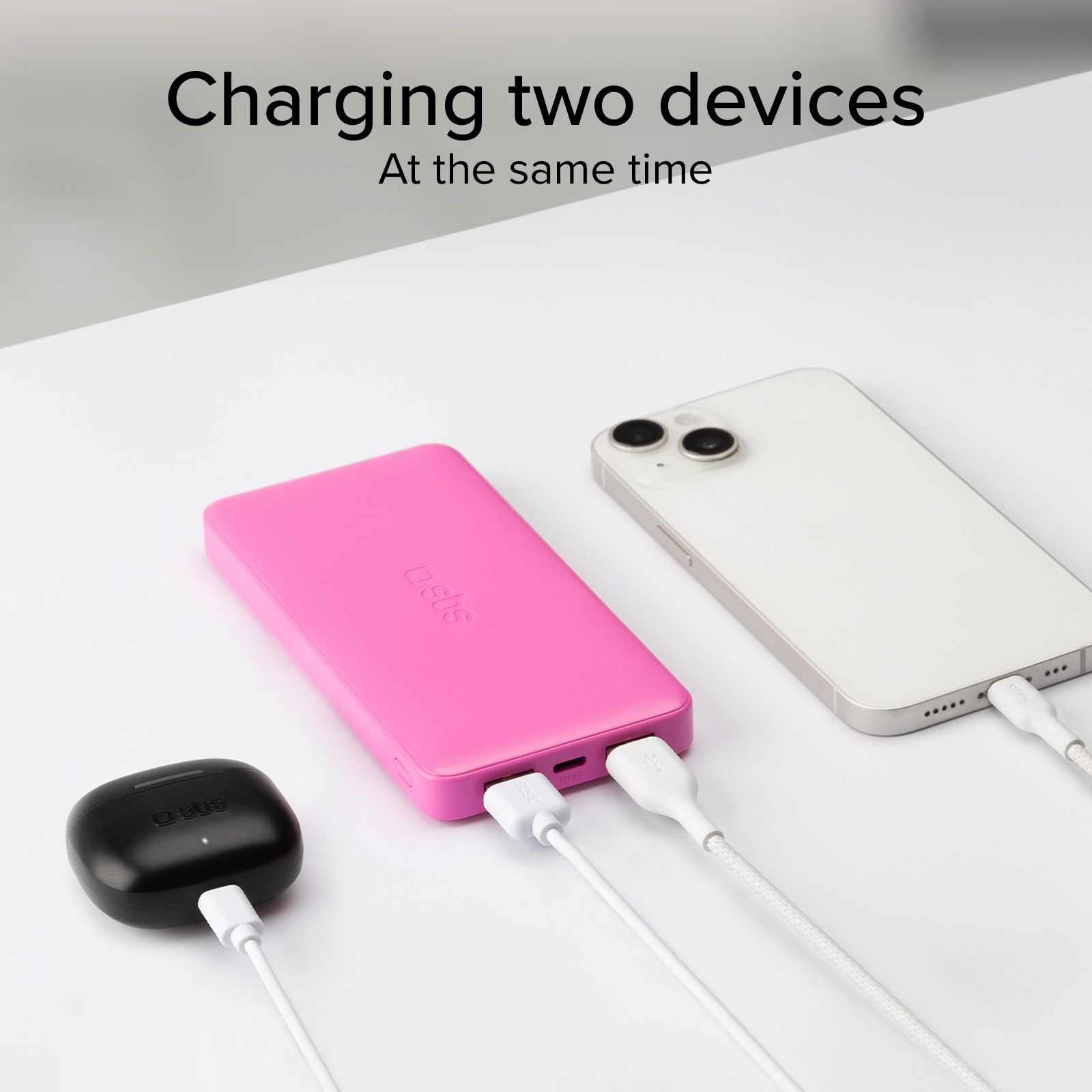 Un power bank rosa, custodia di ricarica nera e smartphone bianco in carica.