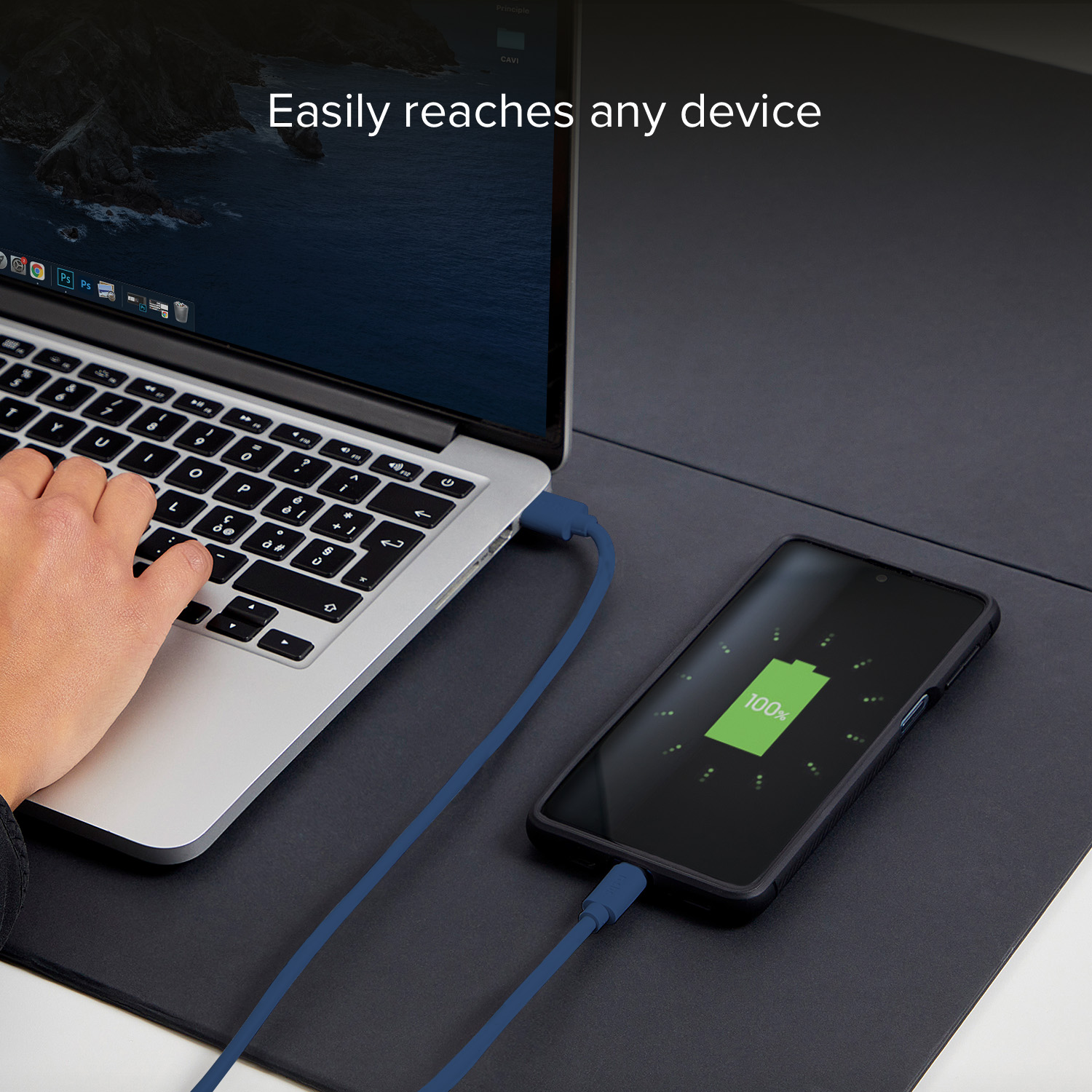 Una mano digita su un laptop. Un telefono collegato da cavo blu mostra 100%.