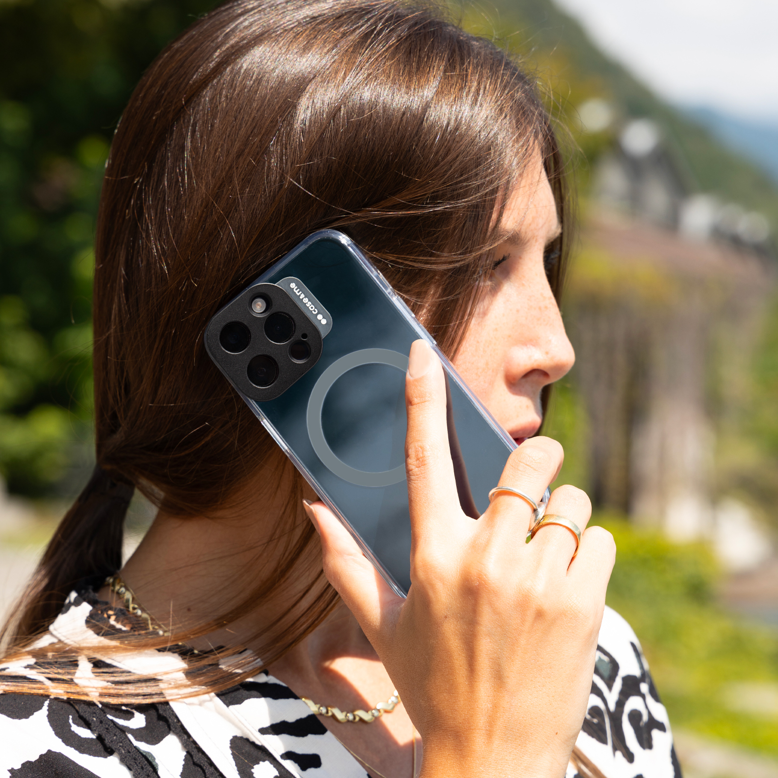 Una mujer sostiene un smartphone en la mano, con un paisaje verde al fondo.