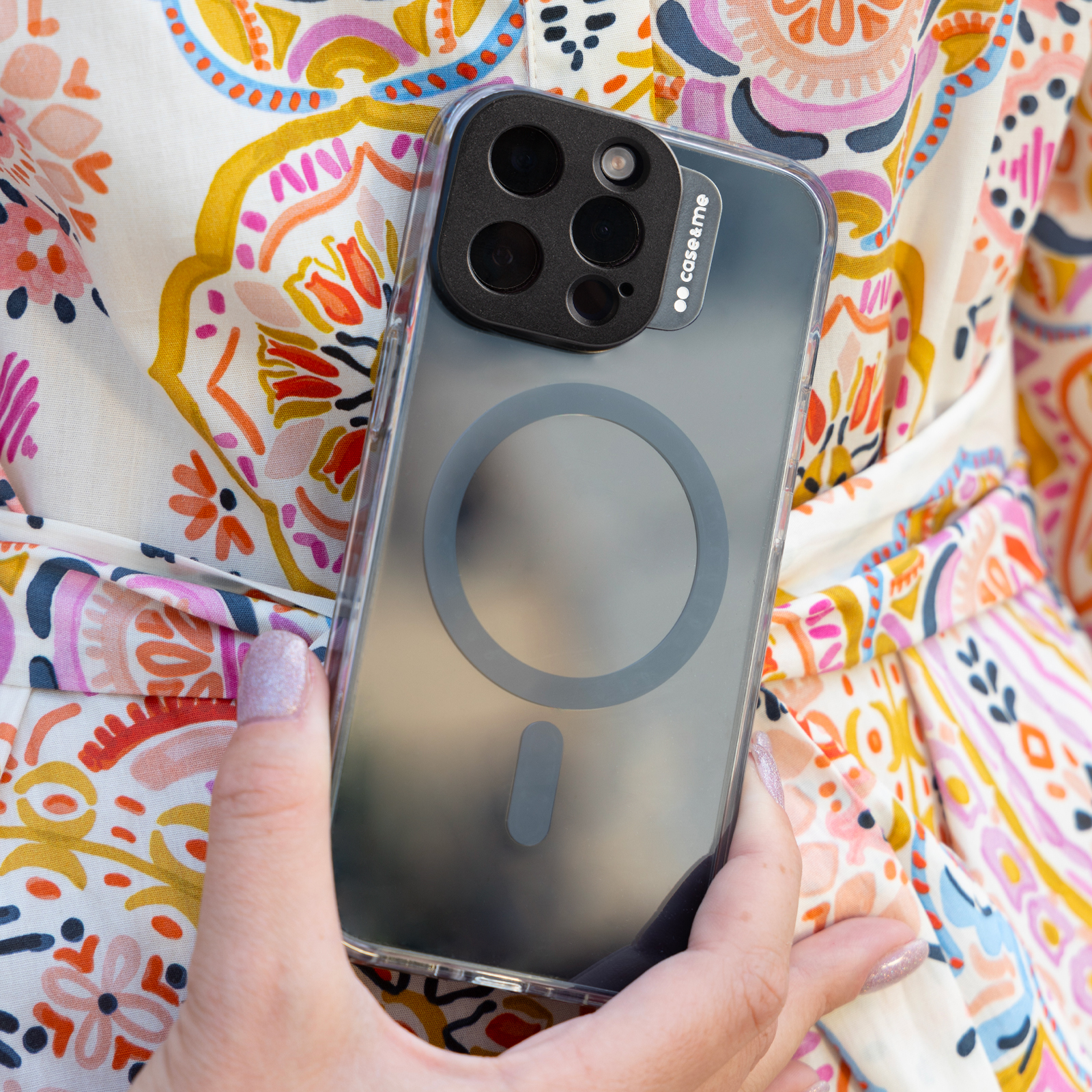 Una mano sostiene un smartphone con funda transparente, ropa colorida.