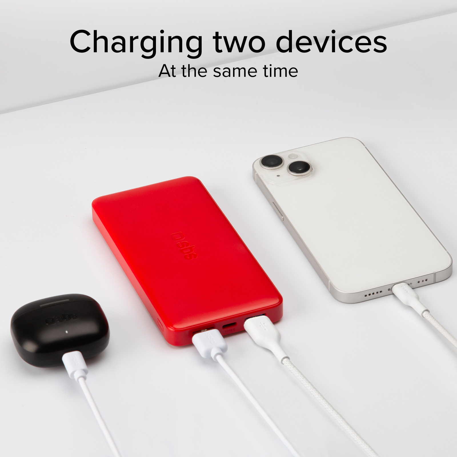 Un power bank rosso carica una custodia per auricolari nera e uno smartphone bianco.