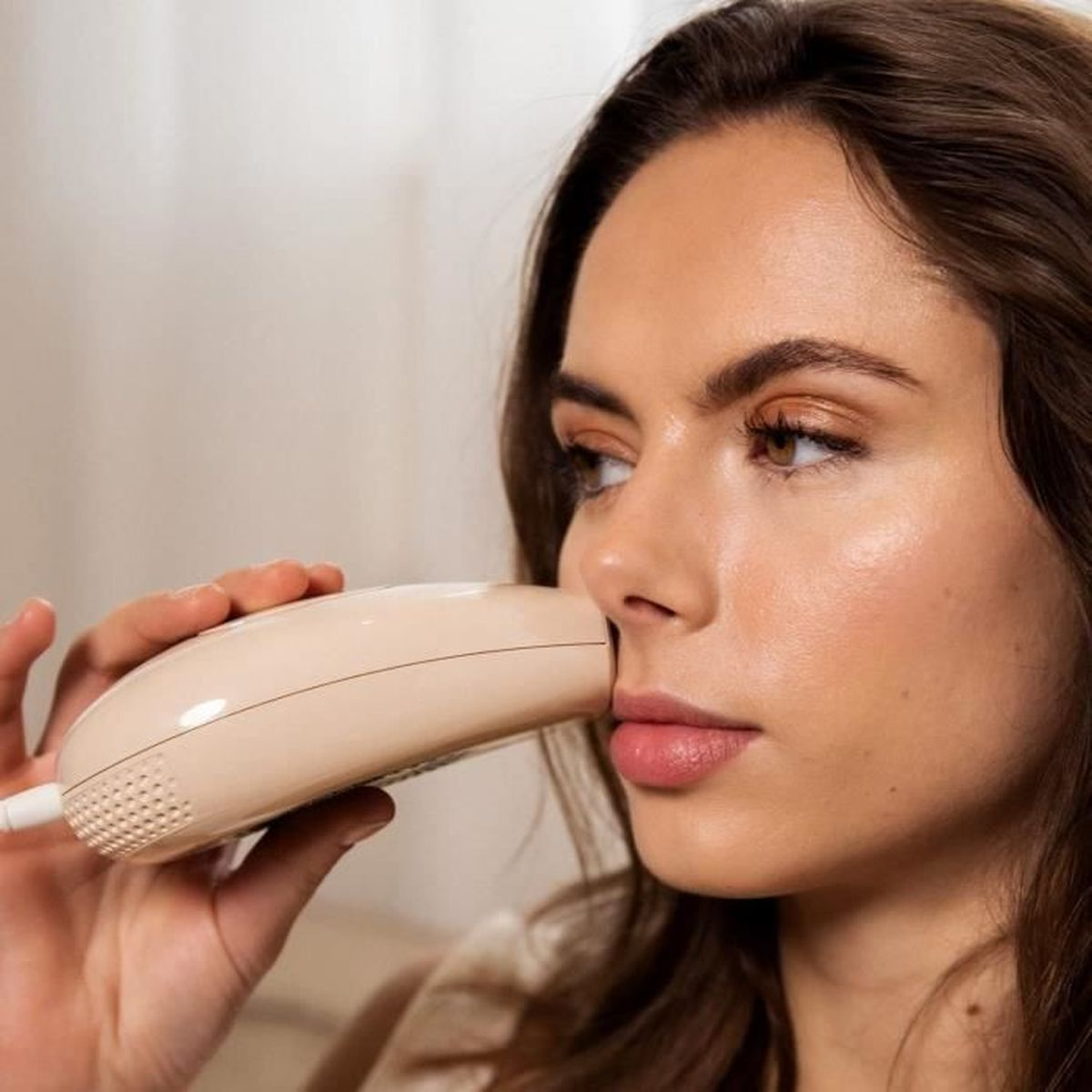 Una donna usa un dispositivo per la cura della pelle del viso beige.