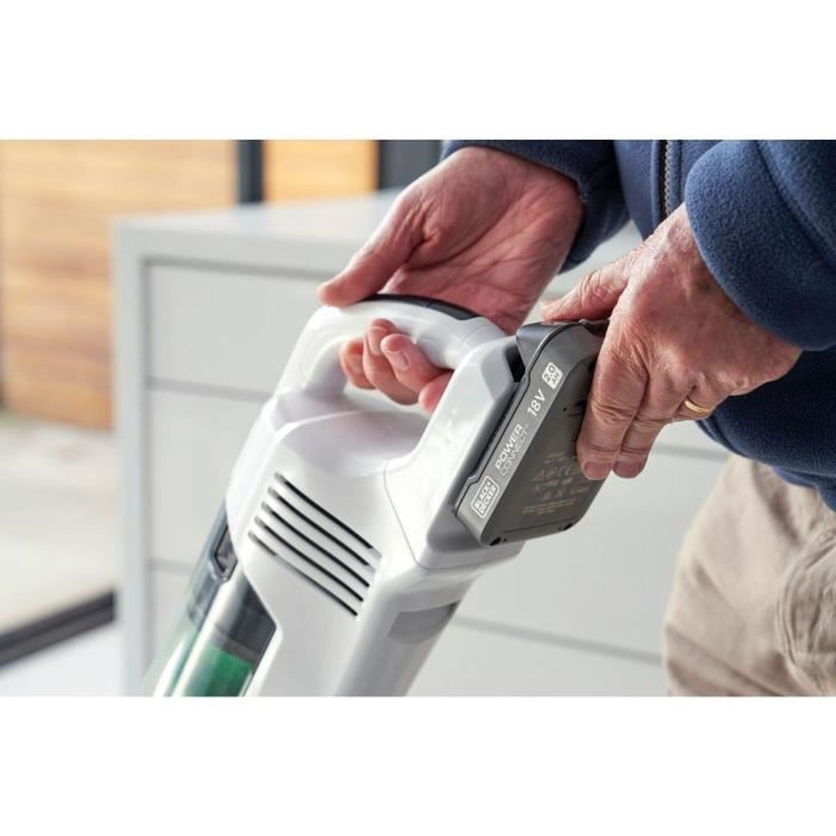 Man inserts a battery into a white handheld vacuum cleaner.