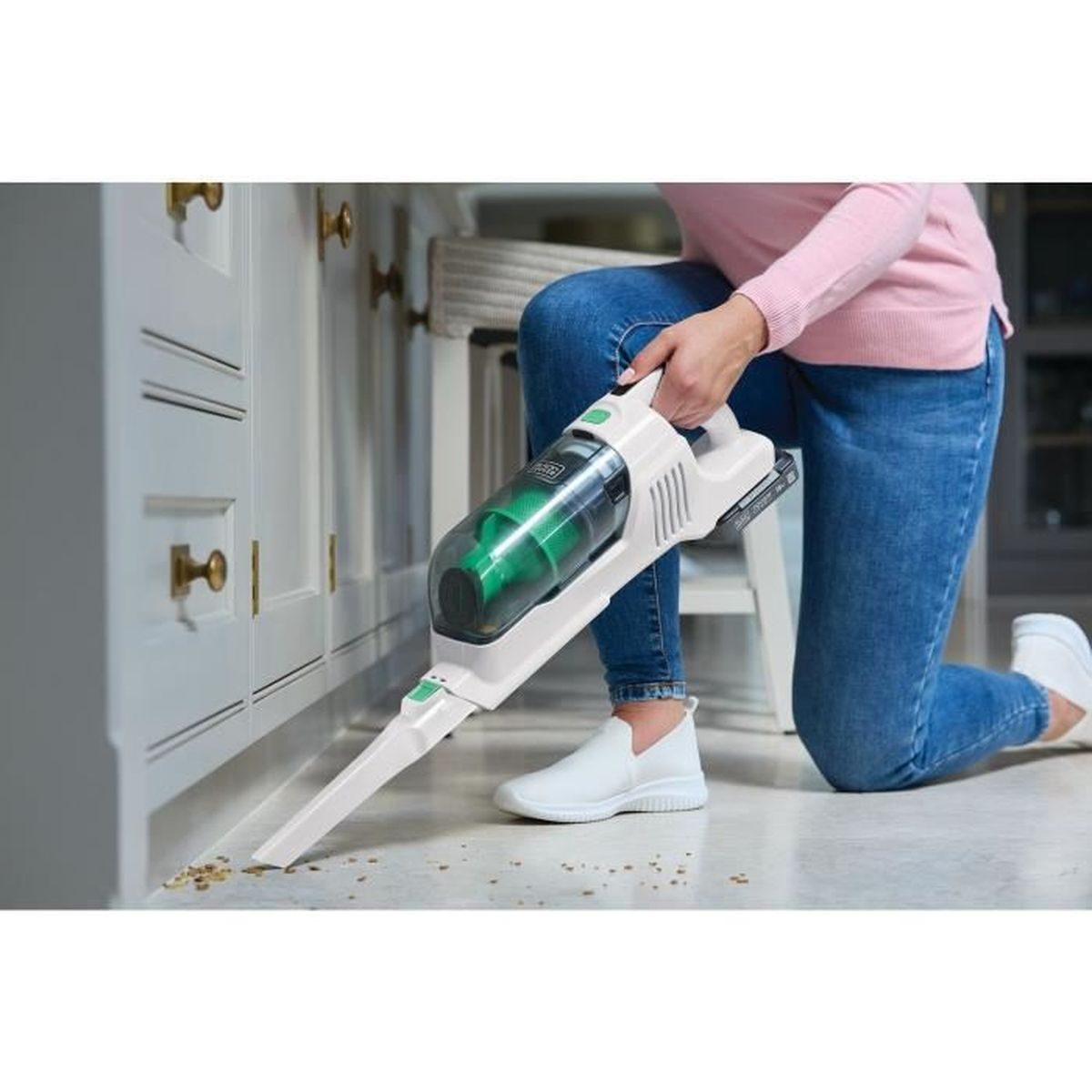 Person in jeans and pink sweater vacuums crumbs with a white handheld vacuum cleaner.