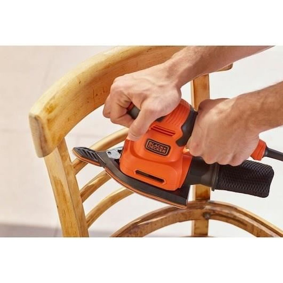 Mani che usano una levigatrice arancione Black+Decker su una sedia di legno.