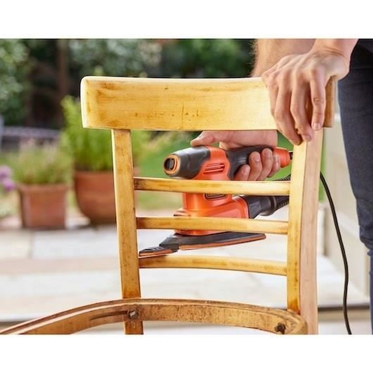 Persona leviga sedia in legno con levigatrice arancione all'aperto.