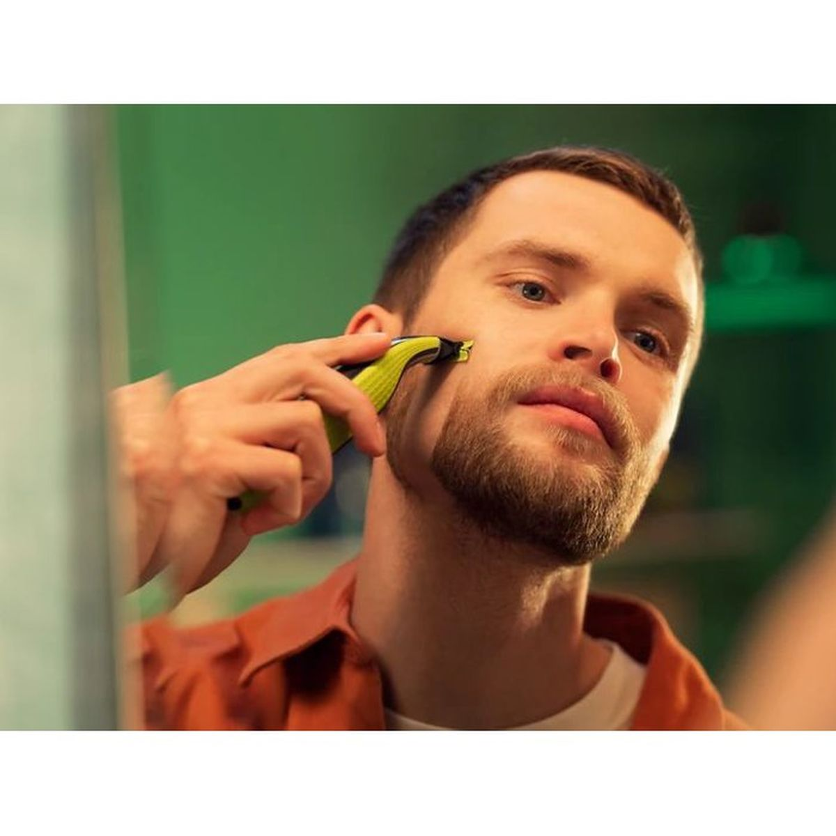 Uomo si rade la barba con un rifinitore giallo su sfondo verde.