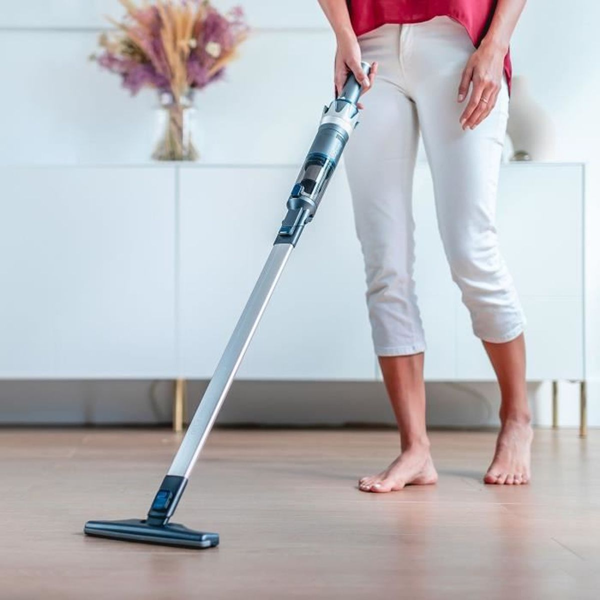 Una persona aspira un pavimento in legno con un aspirapolvere senza fili.
