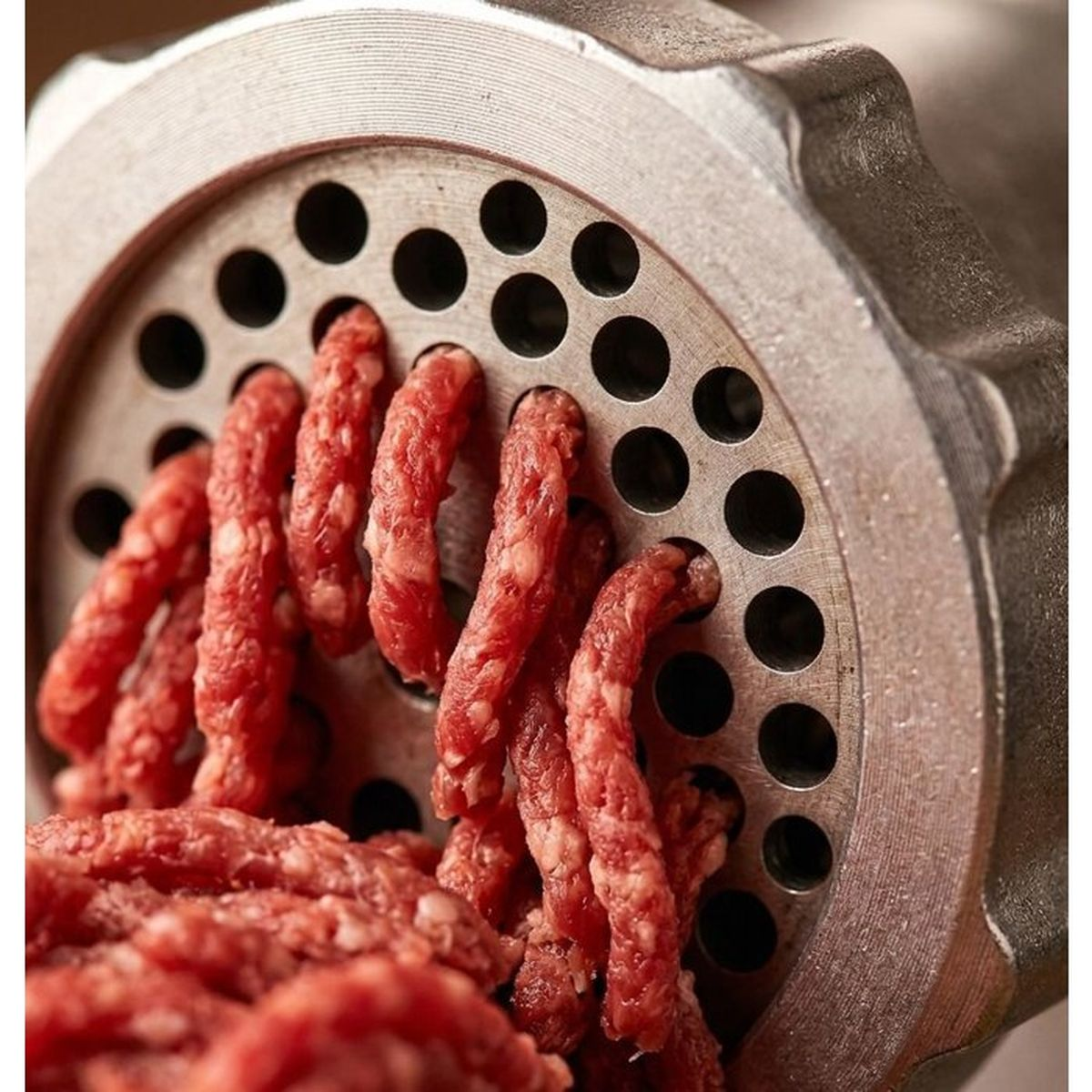 Eine Nahaufnahme eines Fleischwolfs, der Hackfleisch verarbeitet. Rotes Fleisch wird durch die Metallplatte gedrückt.