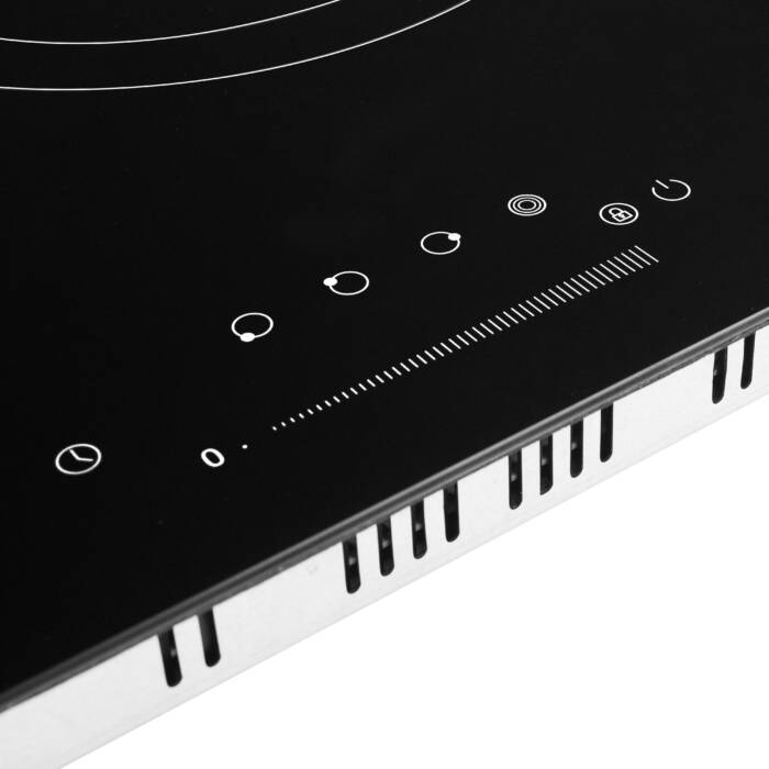 Un piano cottura nero con simboli bianchi e fessure di ventilazione.