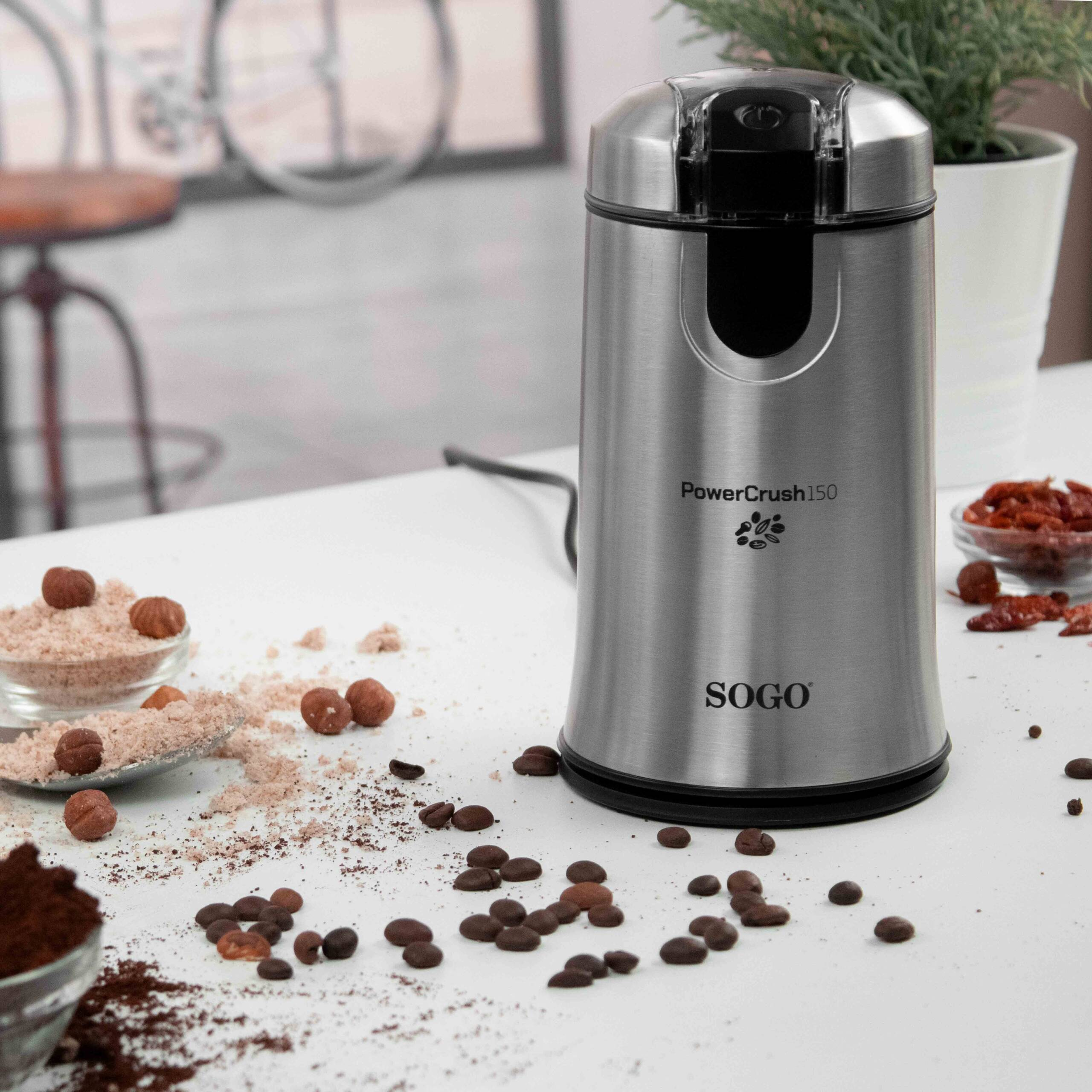 Un molinillo de café plateado está sobre una mesa con granos de café y nueces.