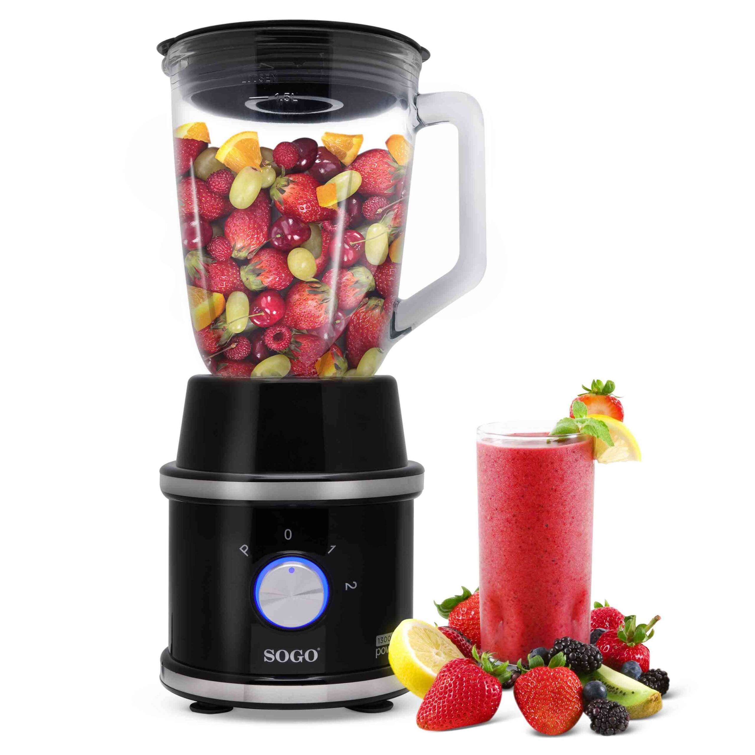 Un frullatore nero pieno di frutta, accanto un bicchiere di frullato e frutti di bosco.