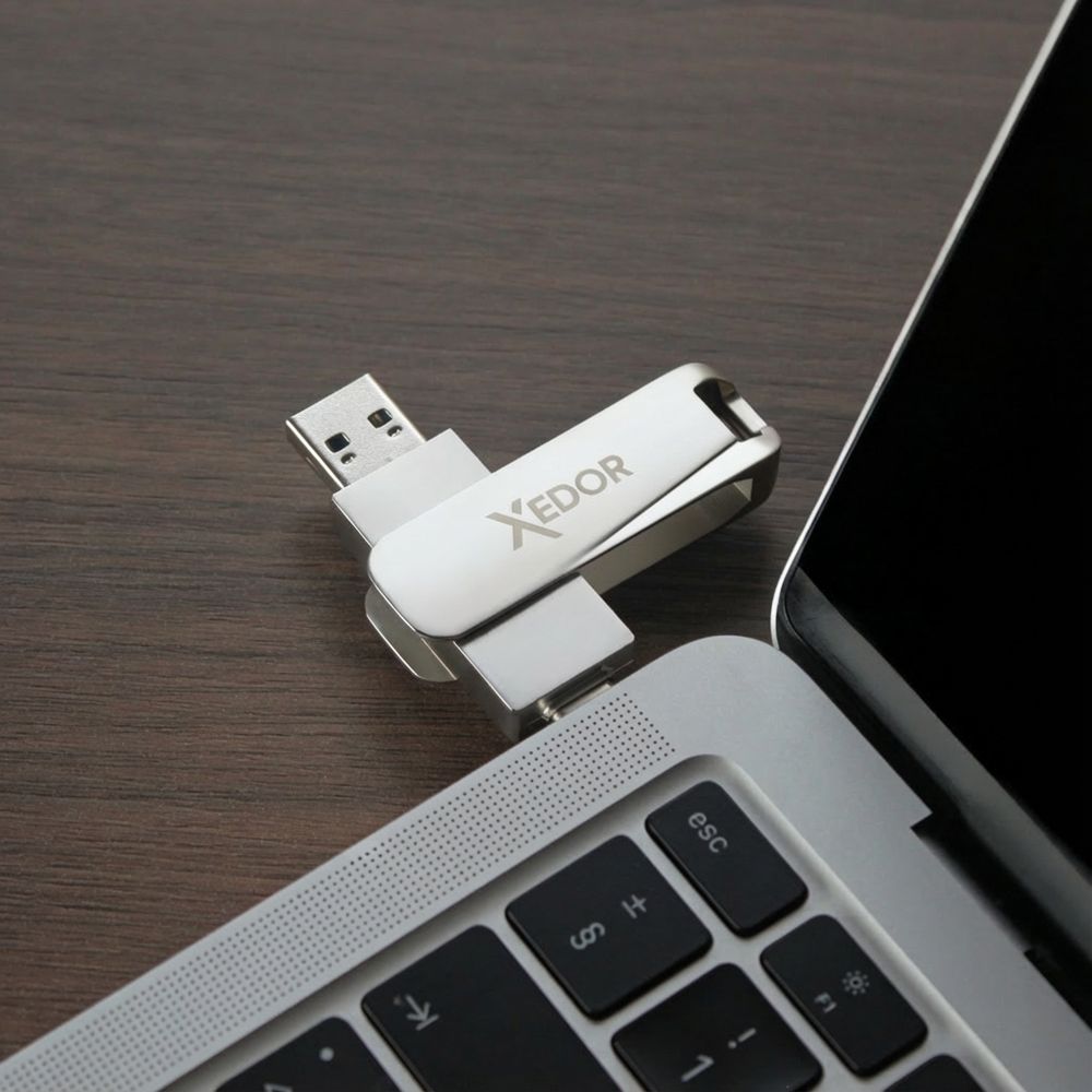 A silver USB drive with the XEDOR logo is plugged into a laptop.