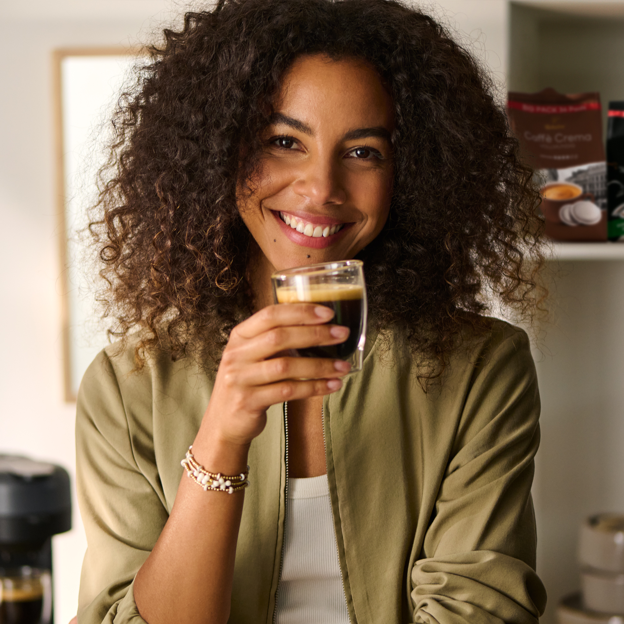 Eine Frau mit lockigem Haar trinkt Espresso aus einem Glas.