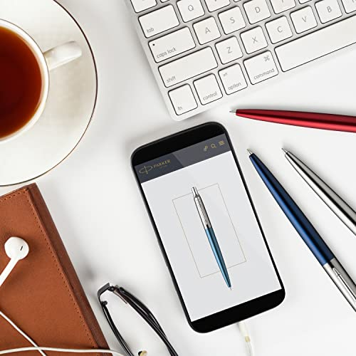 Ein Smartphone zeigt einen Stift, daneben liegen ein Blatt Papier, ein Notizbuch, eine Tasse Tee und Stifte.