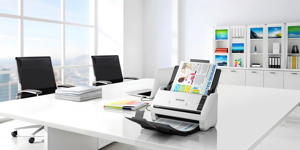Uno spazio ufficio moderno con un grande tavolo, sedie, scanner e laptop.