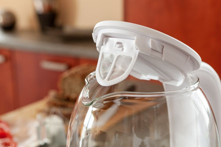Ein offener Wasserkocher aus Glas mit weißem Deckel und integriertem Sieb.