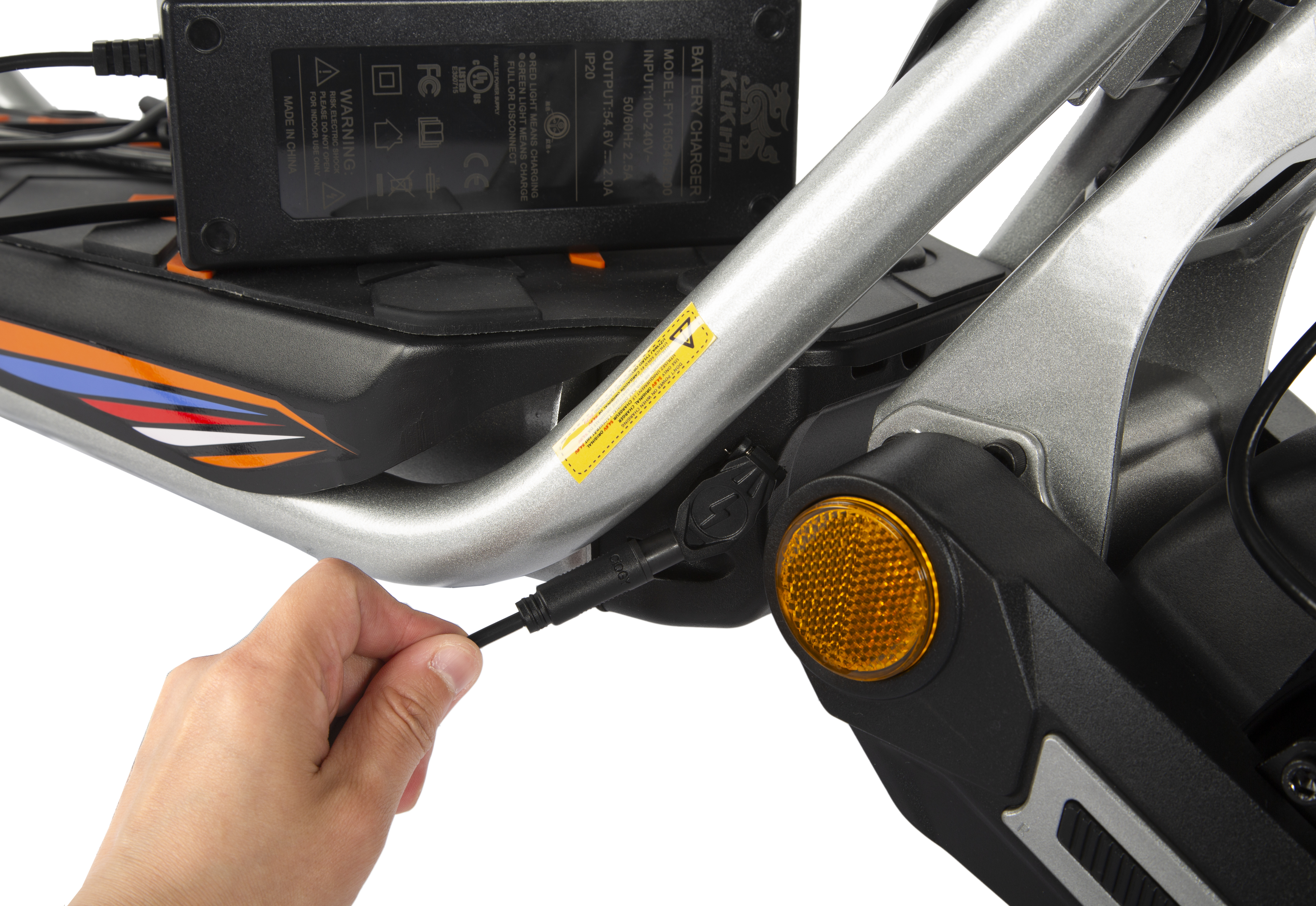 Una mano inserisce un cavo di ricarica in un caricabatterie per e-scooter con etichette di avvertenza.