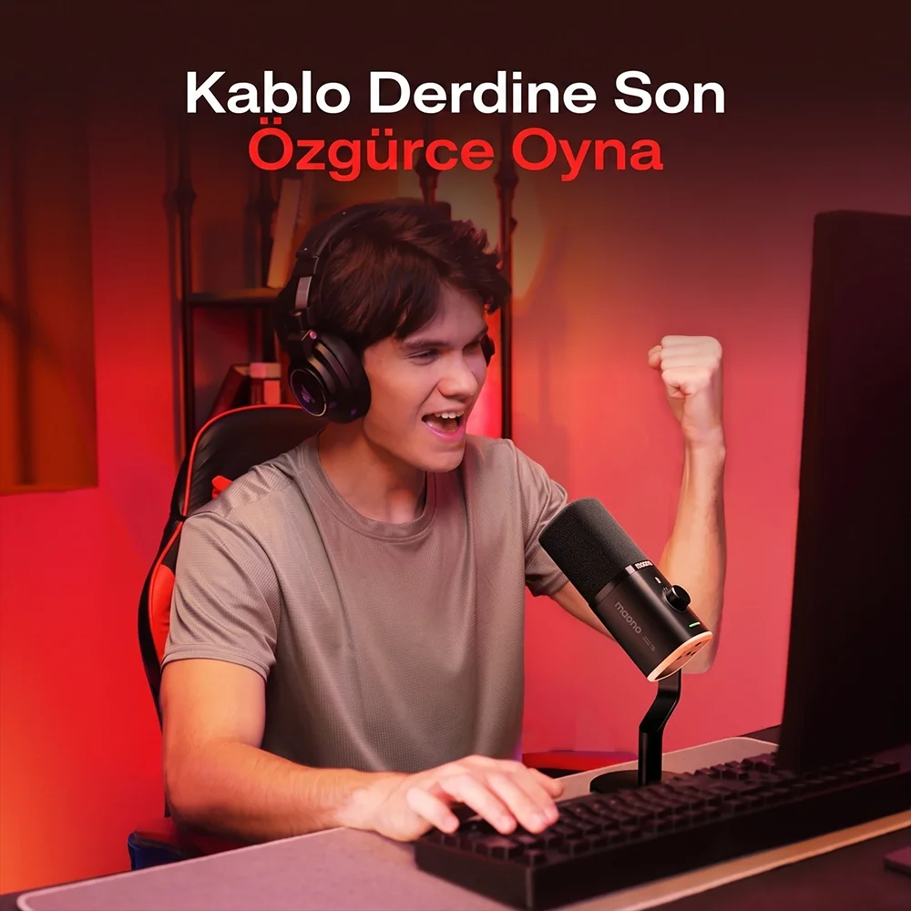 A man wearing headphones sits at a computer, cheering. A microphone is beside him.