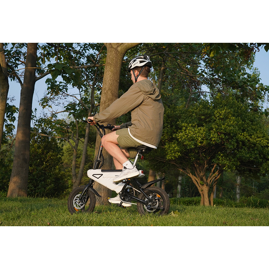 Ein Mann mit Helm fährt ein weißes E-Bike im Gras, umgeben von Bäumen.