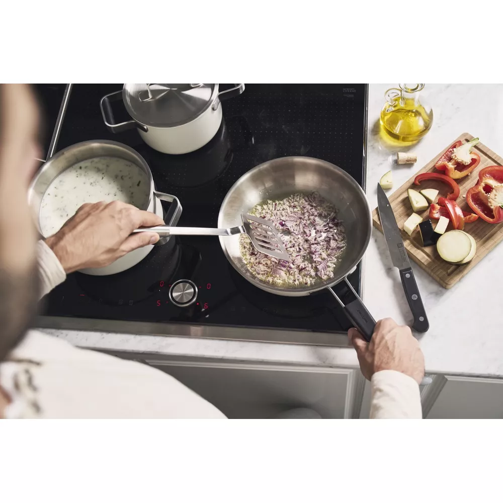 Un hombre cocina cebollas en una sartén en una placa de inducción.