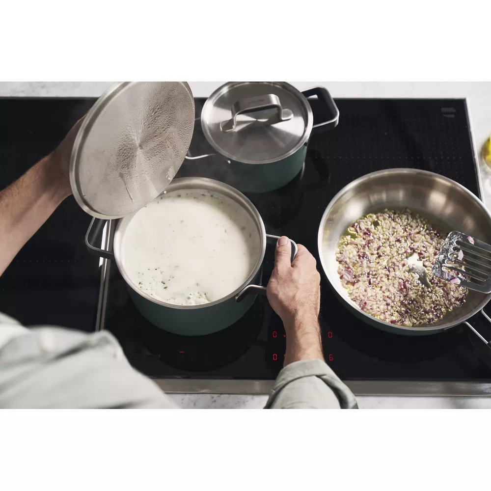 Persona cocinando en placa de inducción con dos ollas y una sartén.