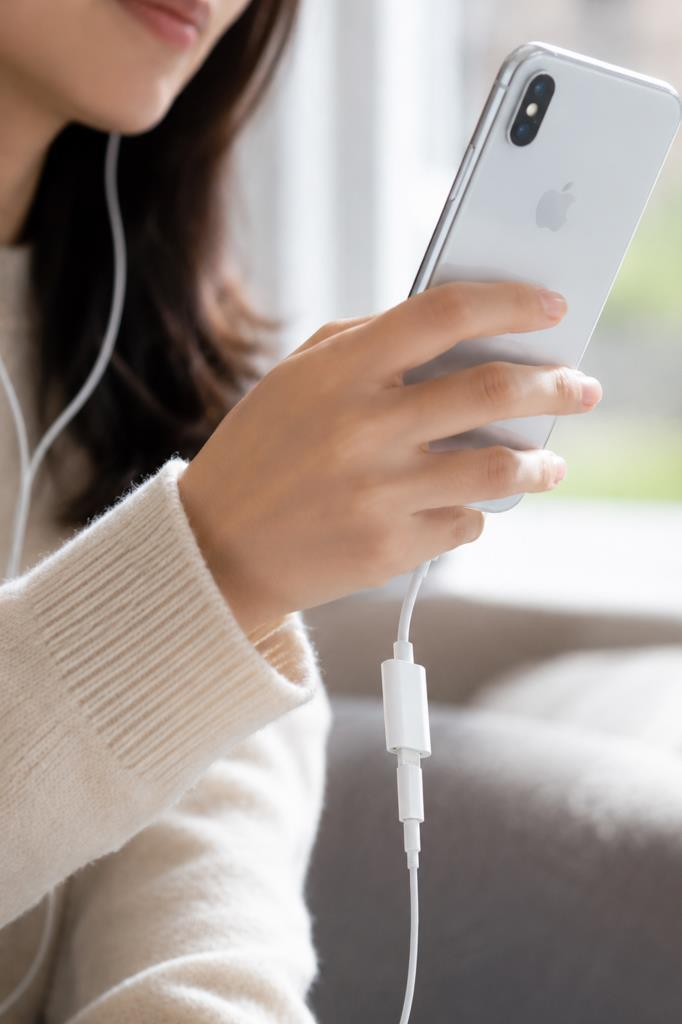 Kulaklık takan bir kişi, adaptöre bağlı gümüş rengi bir iPhone tutuyor.