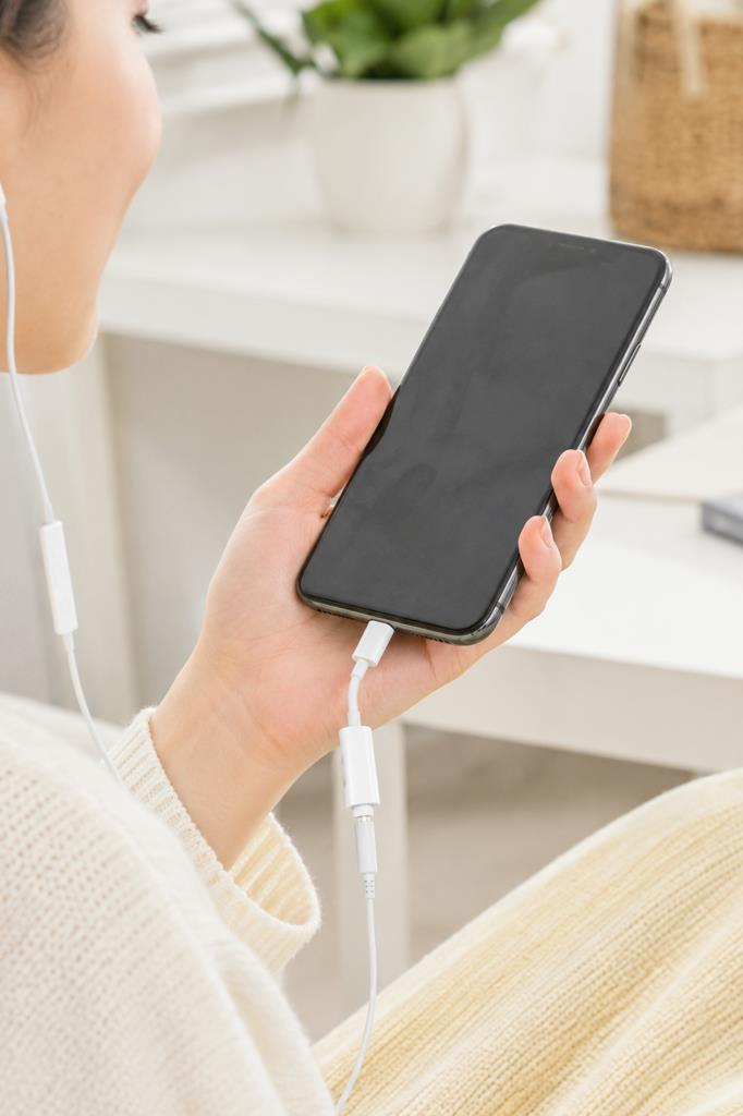 Bir kişi beyaz adaptöre ve kulaklıklara bağlı bir akıllı telefon tutuyor.