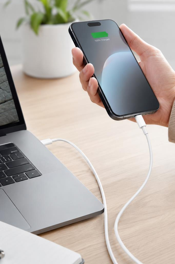 Bir el, beyaz kabloyla dizüstü bilgisayara bağlı bir iPhone tutuyor.