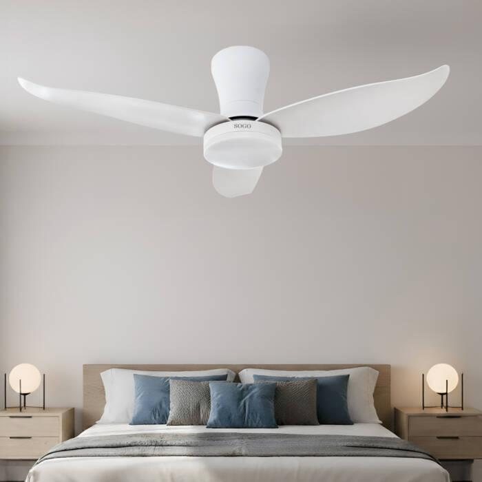 Un ventilatore da soffitto bianco a tre pale pende sopra un letto con cuscini blu e grigi, affiancato da due comodini con lampade.