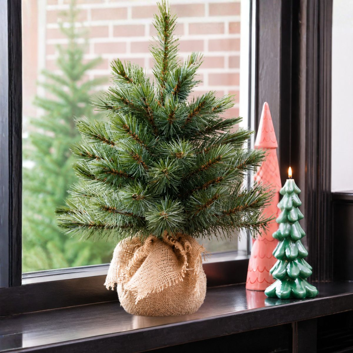 A small pine tree in burlap sits on a shelf next to a lit green tree candle.