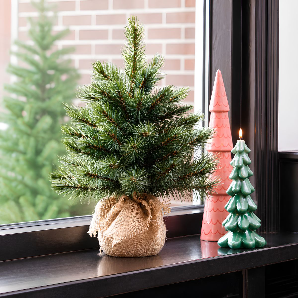 Un petit sapin de Noël en jute, à côté de bougies en forme de sapin roses et vertes.