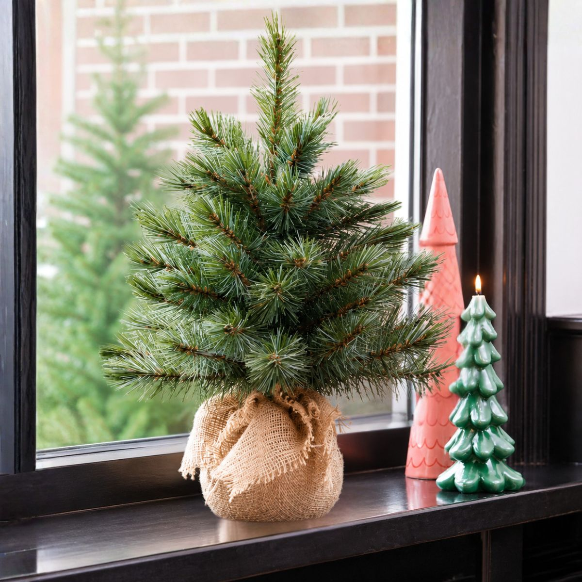 A small Christmas tree in a burlap sack next to a green tree candle.