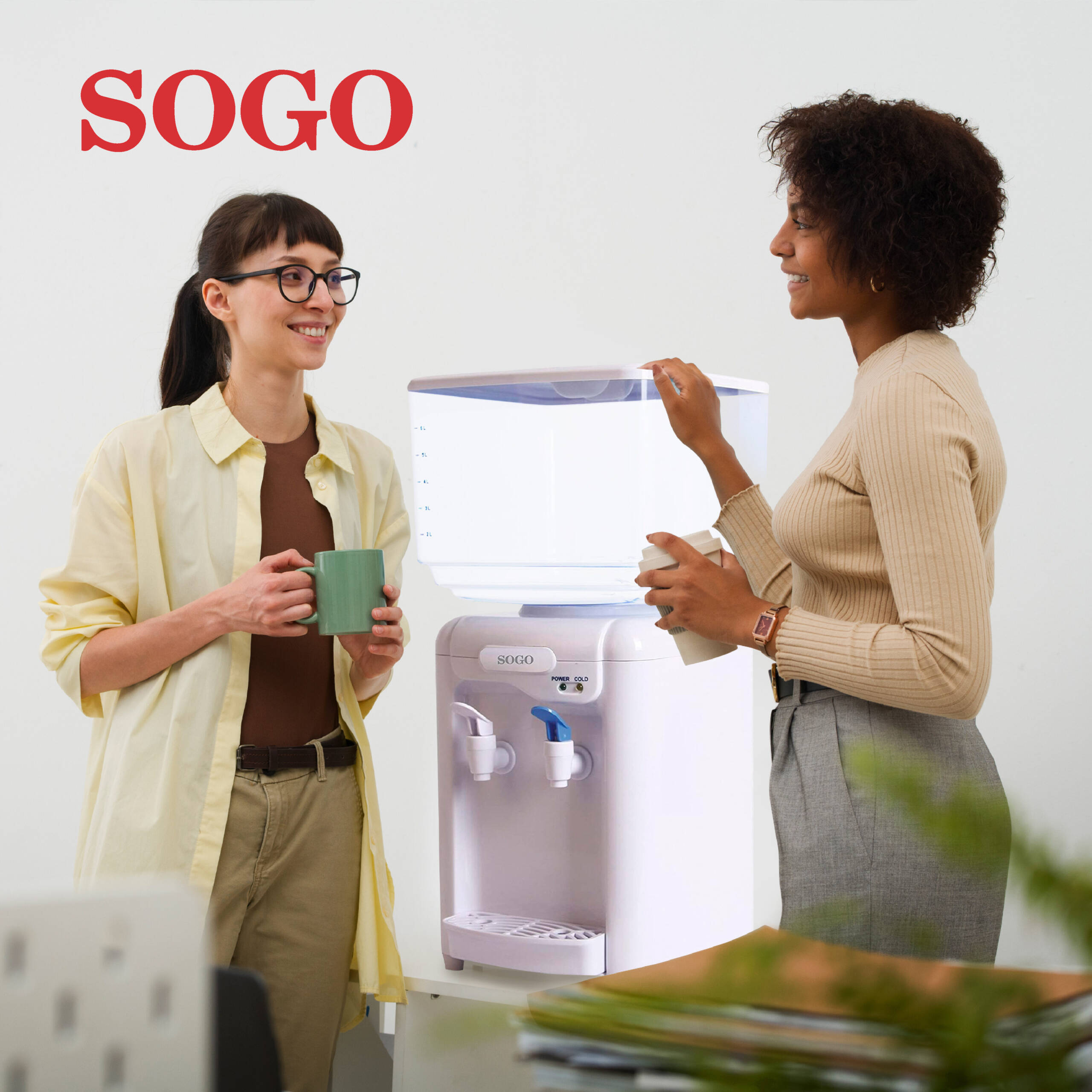 Due donne vicino a un erogatore d'acqua SOGO. Una tiene una tazza, l'altra un bicchiere.