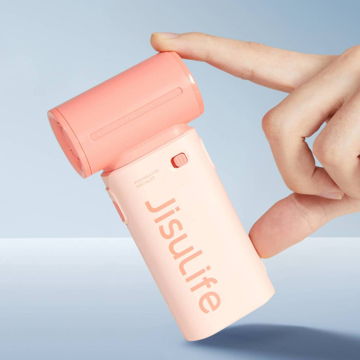 Una mano tiene un ventilatore portatile bicolore in materiali rosa e corallo.