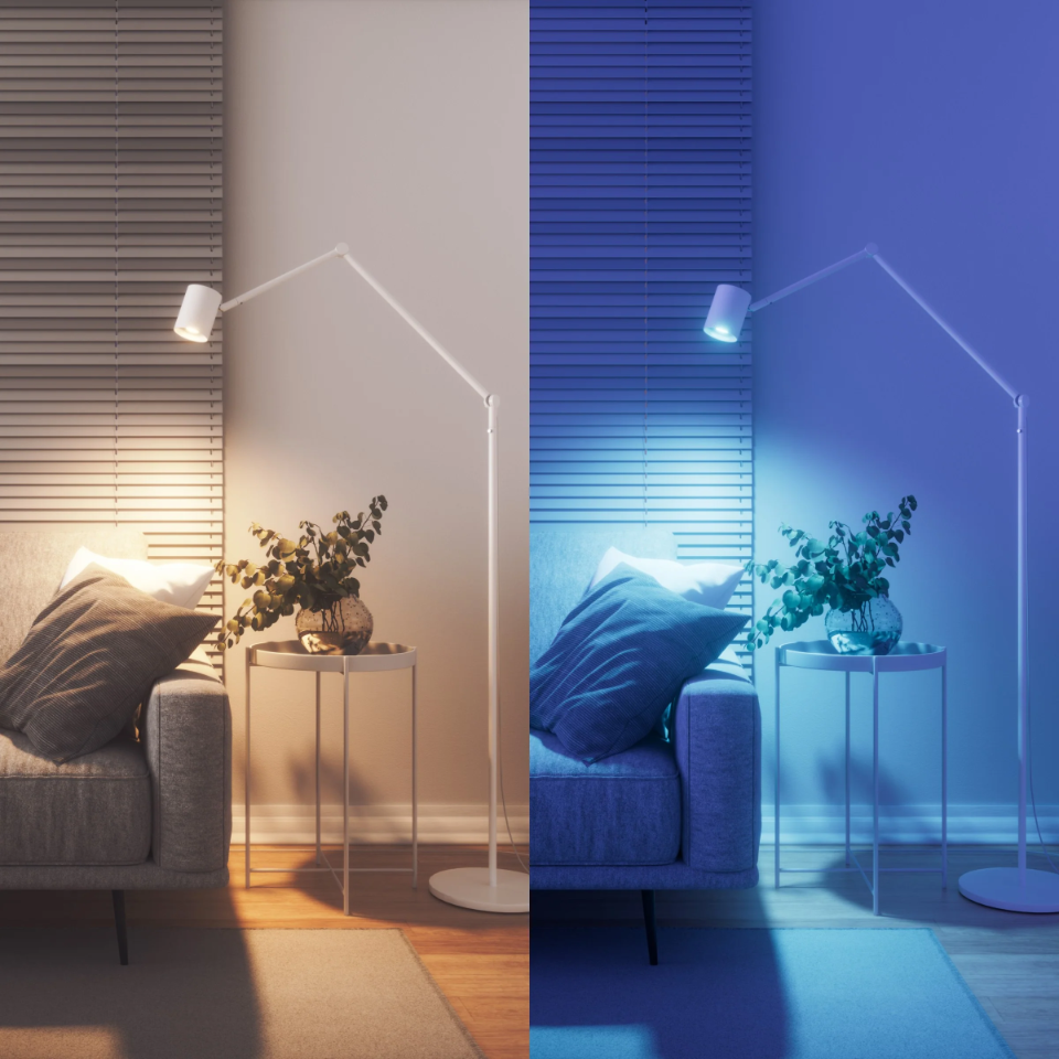 Un soggiorno con divano, tavolino, lampada e piante, illuminato con luce calda e blu.
